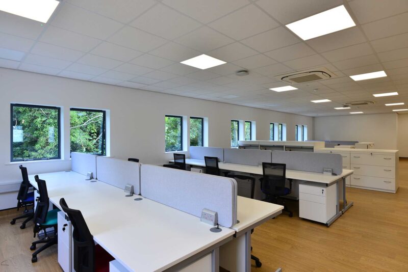 Open plan office in a modular building with white desks, black chairs and wooden flooring.