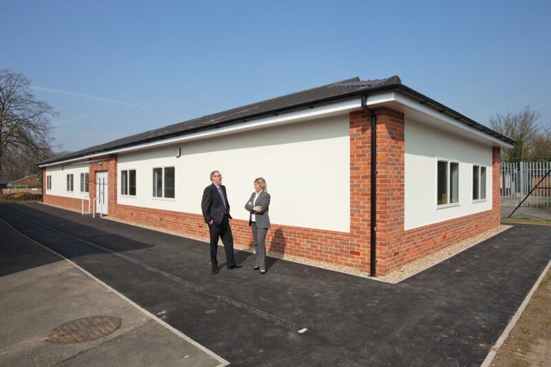 Modular building with a brick base and light exterior, with people standing outside.